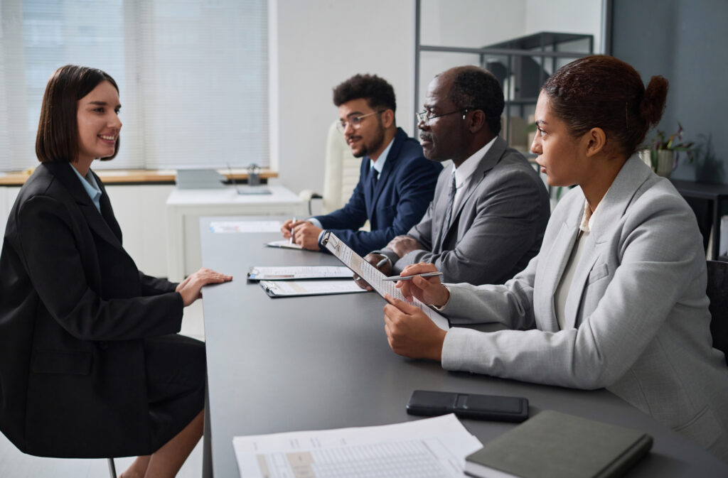 An applicant answering job interview questions in the front or three recruiters.